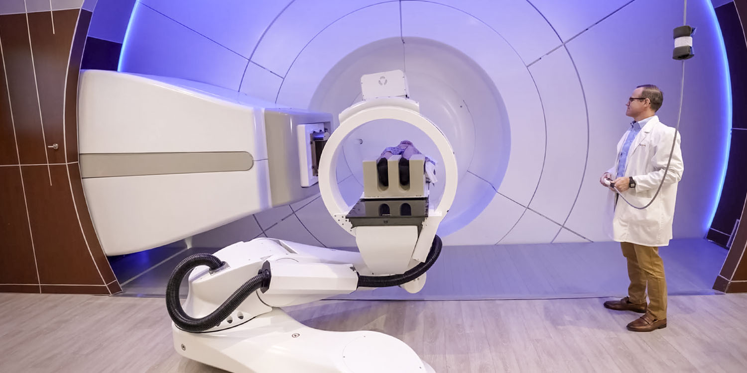 A patient lays on the proton therapy treatment table while therapist adjusts positioning