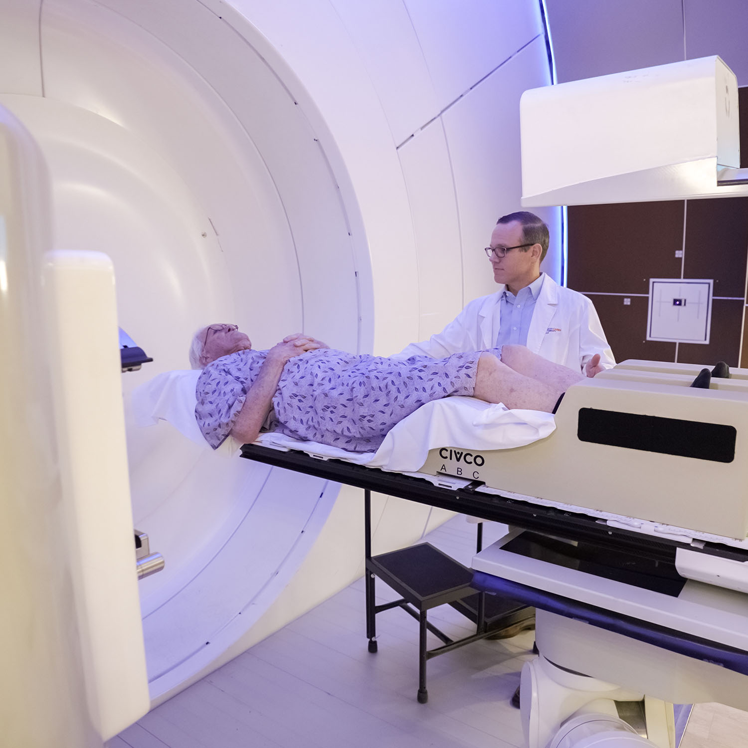 Prostate cancer patient lays on treatment table while radiation therapist aligns him for proton therapy